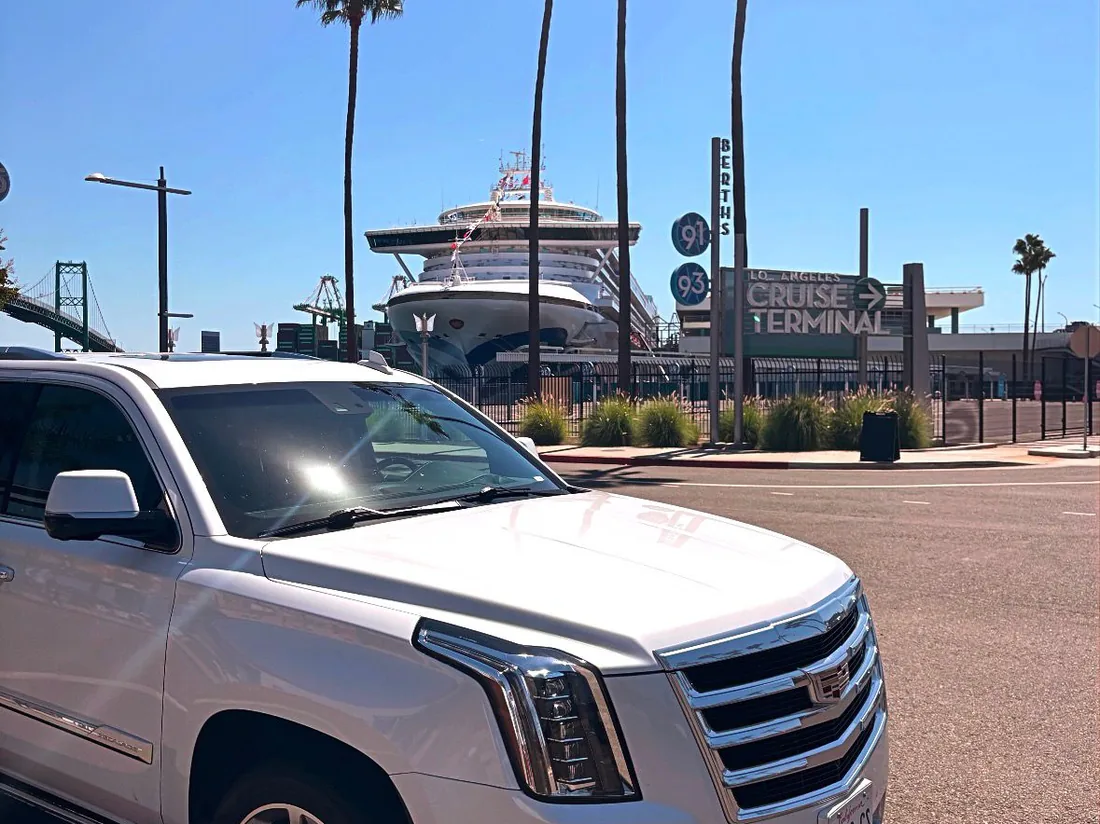 White luxury SUV in front of the Los Angeles Cruise Terminal at San Pedro with a cruise ship behind